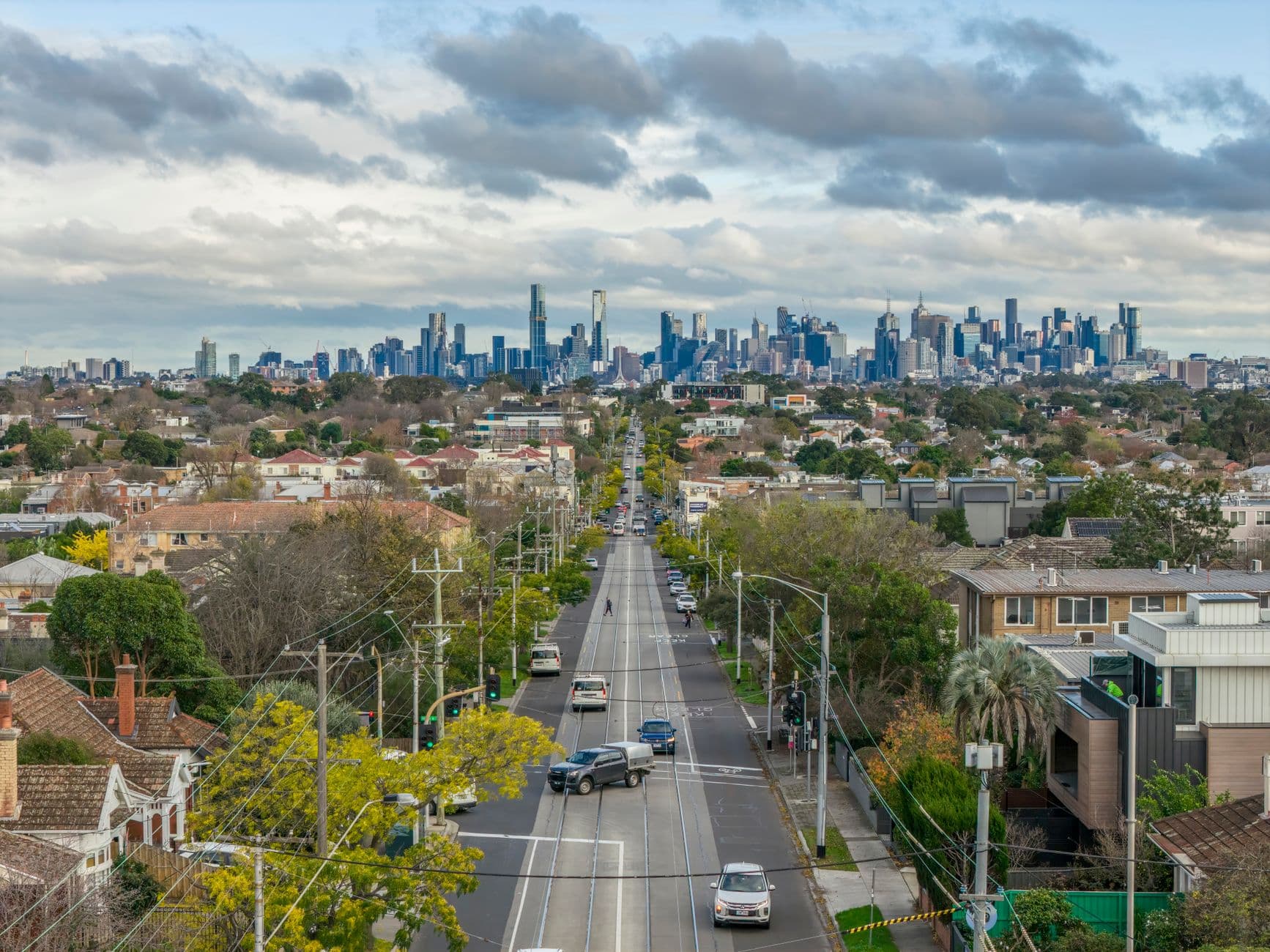 An expansive view of Melbourne's suburban road leading to the city skyline with lush greenery and overcast skies.